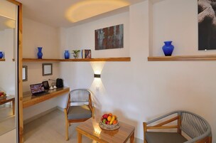 Una habitación con un escritorio de madera, dos sillas, una computadora portátil, un frutero y un estante en la pared con objetos decorativos.