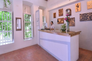 Zona de recepción con una recepcionista, un mostrador de madera y obras de arte en las paredes.