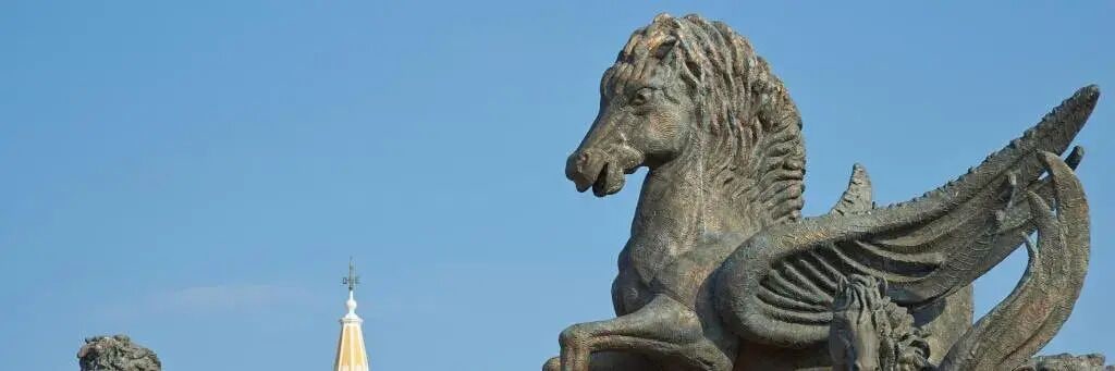 Eine Steinskulptur eines Reiters auf einem Pferd vor blauem Himmel.