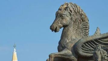 Eine Steinskulptur eines Reiters auf einem Pferd vor blauem Himmel.