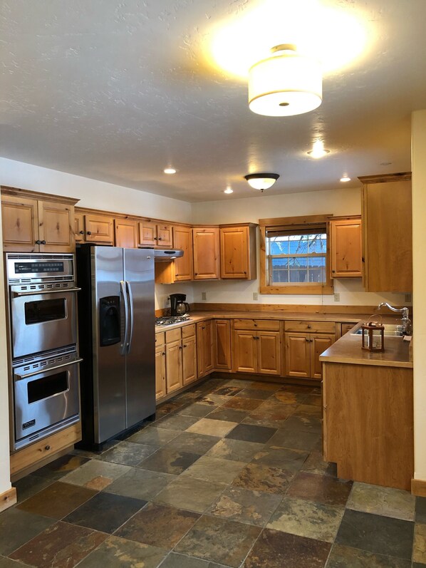 A kitchen with wooden cabinets, a stainless steel refrigerator, an oven, and a window.