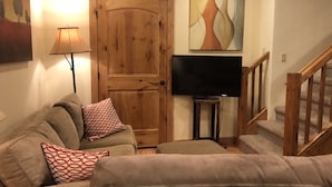 Uma sala de estar com porta de madeira, sofá, televisão e escada.