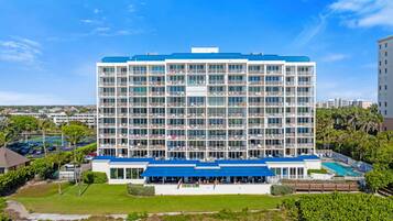 A multi-story hotel with a blue roof, a pool area, and a view of the surrounding landscape.