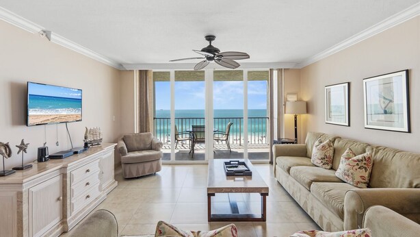 Un salon équipé d’un téléviseur, d’un ventilateur de plafond, d’un canapé, d’une table basse et offrant une vue sur la plage.