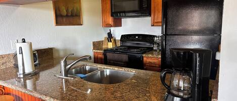 A kitchen with granite countertops, stainless steel appliances, wooden cabinets, and a black refrigerator.