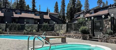 A swimming pool with a stone deck, surrounded by a stone wall and a metal fence.
