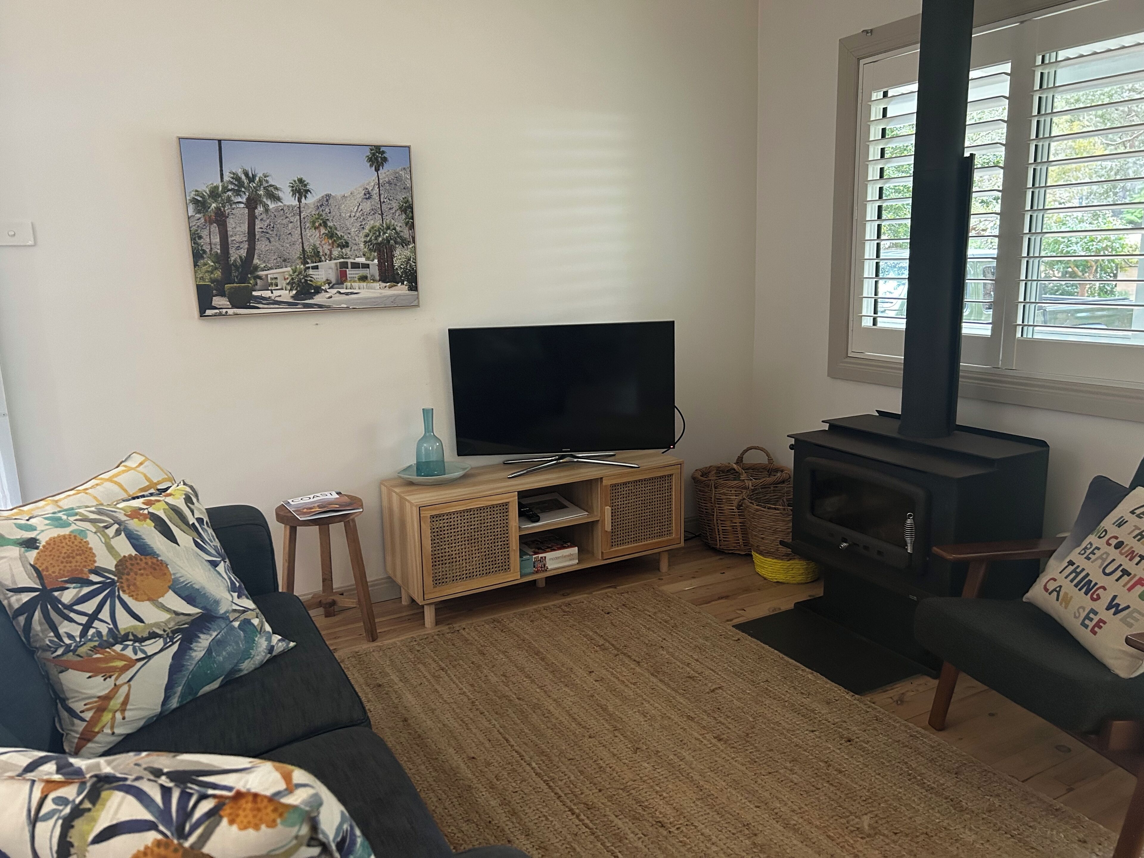 A living room with a sofa, a TV on a wooden stand, a painting on the wall, and a wood-burning stove.