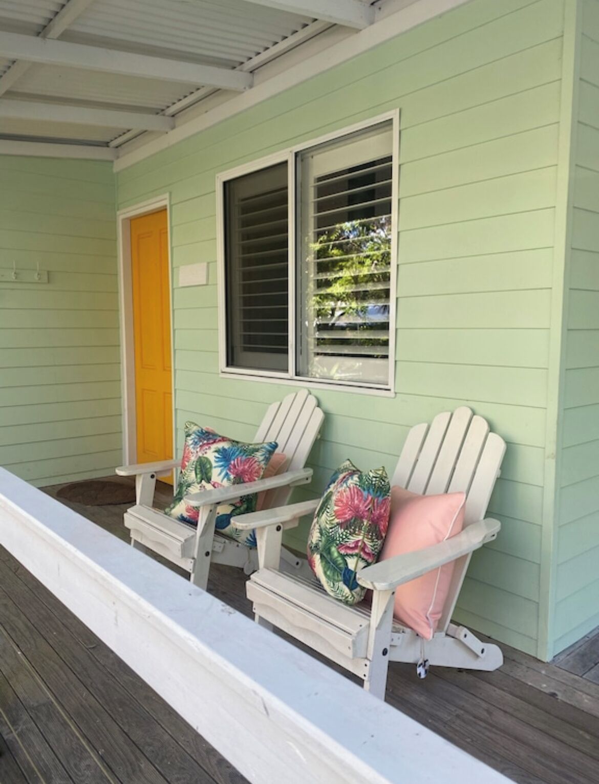 A porch with two Adirondack chairs, a yellow door, and a window with blinds.