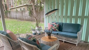 A covered outdoor seating area with wicker furniture, a wooden table, and potted plants.