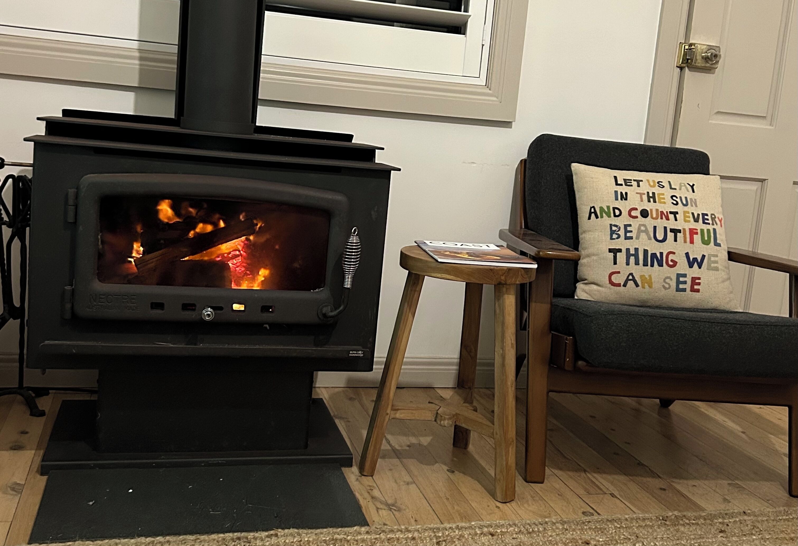 A wood-burning stove in a living room with a cozy chair and a decorative pillow.