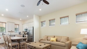 Una sala de estar moderna con un sofá beige, una mesa de centro de madera y una zona de comedor con una mesa y sillas blancas.