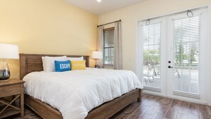 Un dormitorio con una cama de madera, dos mesitas de noche, un ventanal con persianas y vistas al exterior.