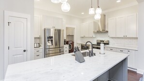 Une cuisine moderne avec des meubles blancs, des appareils en acier inoxydable et des luminaires suspendus.