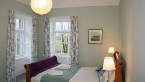 Un dormitorio con una cama, una mesita de noche, una lámpara y una ventana con cortinas.
