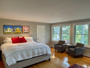 Une chambre à coucher avec un grand lit, deux fauteuils et une fenêtre donnant sur les arbres.