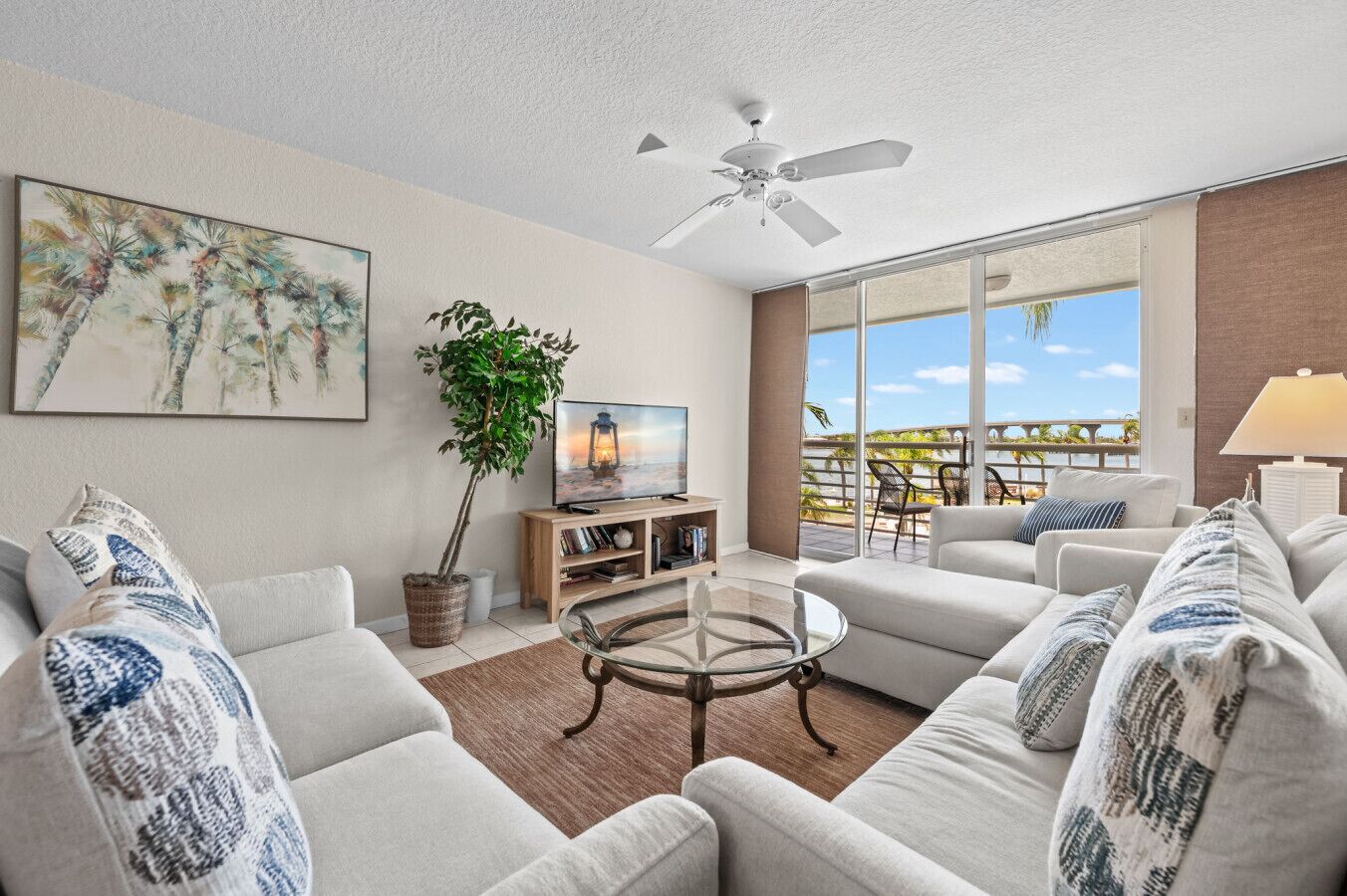 A spacious living room with a large sofa set, a coffee table, a television, and a balcony with a view.