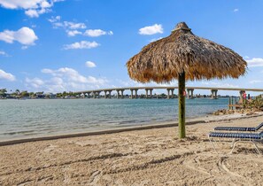 Ein Strand mit einem Reetdachschirm, Liegestühlen und einem Steg im Hintergrund.