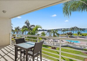 Ein Balkon mit Korbmöbeln, ein Pool und der Blick auf eine Brücke und Palmen.