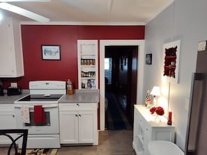 Une cuisine avec des meubles blancs, un four et un plan de travail. Un mur est peint en rouge et un couloir mène à une autre pièce.