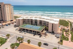 A multi-story hotel with a rooftop tennis court, parking garage, and a view of the ocean.