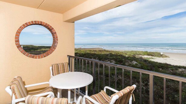A balcony with a round brick window, white chairs, and a small table.