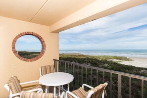 A balcony with a round brick window, white chairs, and a small table. - Suntide II 204 - Beachfront Direct Ocean View and Beach Access, Pool, Hot Tub and More (South Padre Island)