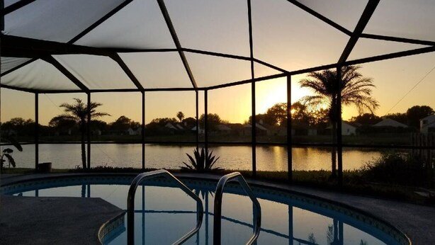 A swimming pool with a clear view of the sunset over a lake, surrounded by palm trees and a covered area. - Spacious & amazing lake view with pool.  (Brandon)