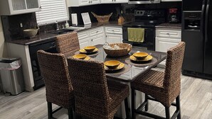 A modern kitchen with white cabinets, a black refrigerator, a microwave, and a dining table with wicker chairs. - Spacious & amazing lake view with pool.  (Brandon)