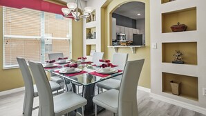 Comedor con mesa de vidrio dispuesta para seis personas, sillas blancas y camino de mesa rojo y blanco.
