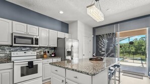 Cocina moderna con armarios blancos, encimeras de granito, electrodomésticos de acero inoxidable y una isla grande con taburetes de bar.