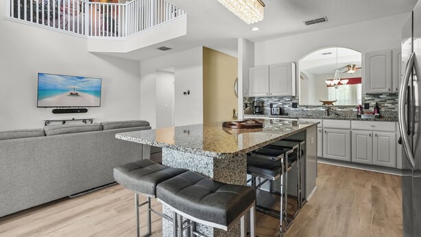Una cocina moderna con una isla central, taburetes de bar y una zona de comedor con un sofá gris.