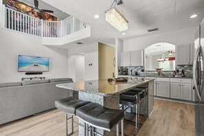 Een moderne keuken met een centraal eiland, barkrukken en een zithoek met een grijze bank.