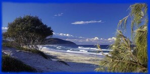A beach with clear skies, waves, and a distant mountain.