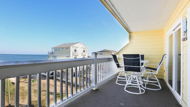 Ein Balkon mit Blick auf Strand und Meer, weiße Gartenmöbel und eine gelbe Wand.