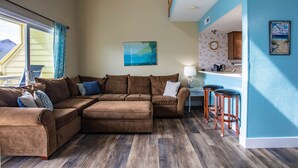 Ein Wohnzimmer mit Ecksofa, einer kleinen Küchenzeile und einer Essecke mit Barhocker.