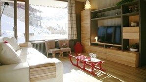 Ein gemütliches Wohnzimmer mit einer Couch, Sesseln, einem Fernseher und einem Holzschrank.