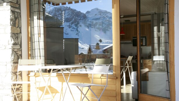 Eine Holzterrasse mit Tisch und Stühlen, eine Glastür zum Küchenbereich und Blick auf die Berge.