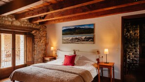 Een gezellige slaapkamer met een stenen muur, houten balken, een bed met een rood kussen en een schilderij van bergen.