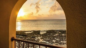 Une vue à travers une fenêtre en arc donnant sur une côte rocheuse au coucher du soleil.