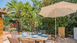 An outdoor dining area with a wooden table set for six, surrounded by chairs, under a large umbrella. - High Quality Designer Detached Villa from Artist Sculptor owner Miquel Cerda (Pollensa)