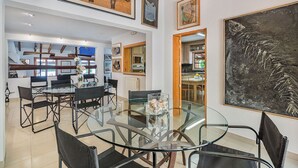 A modern dining area with a glass table and black chairs, a kitchen in the background, and various artworks on the walls. - High Quality Designer Detached Villa from Artist Sculptor owner Miquel Cerda (Pollensa)