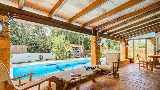 An outdoor patio with a pool, wooden furniture, and a view of the surrounding greenery. - High Quality Designer Detached Villa from Artist Sculptor owner Miquel Cerda (Pollensa)