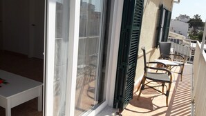 Un balcón con mesa y sillas, una puerta corrediza de vidrio y vistas de los edificios circundantes.