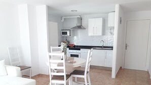 Una cocina moderna con armarios blancos, un microondas y un fregadero. Hay una mesa de comedor con sillas y un sofá blanco en la sala de estar.