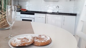Una cocina moderna con armarios blancos, encimera negra y una mesa de comedor blanca con dos pasteles y un vaso de agua.