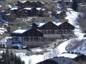 Un ensemble de chalets de montagne en bois, dotés de plusieurs balcons, niché au milieu de pentes enneigées.