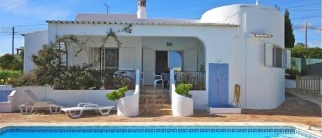 A white villa with a swimming pool, a covered patio, and a small garden area.