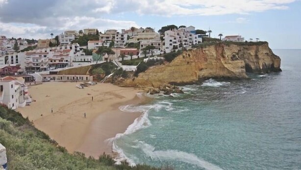 Uma vila costeira com edifícios construídos num penhasco com vista para uma praia.