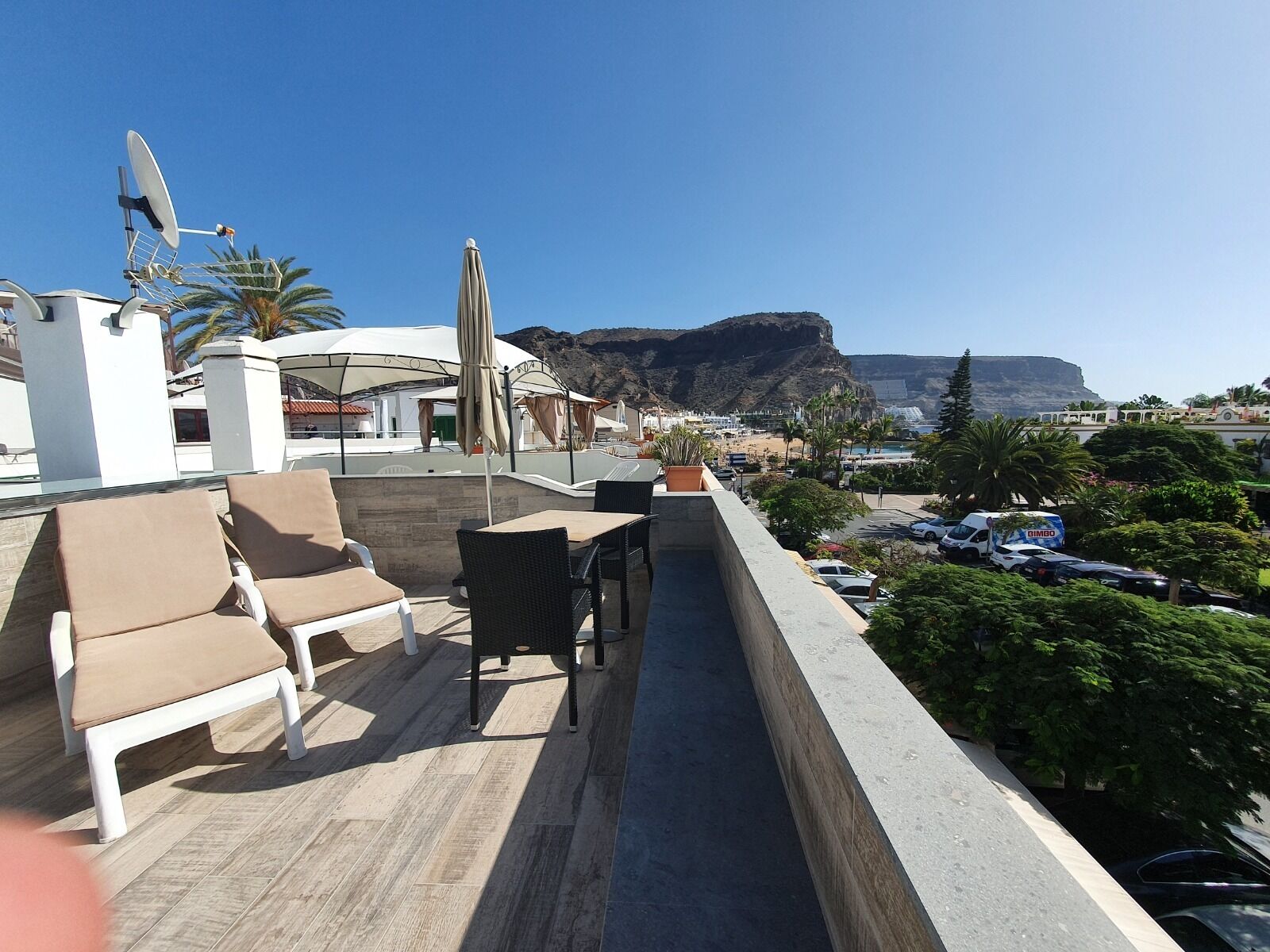 A rooftop terrace with lounge chairs, umbrellas, and a view of the coastline.