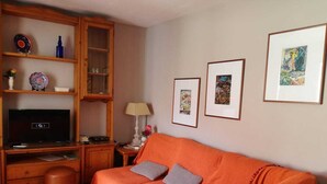 Een woonkamer met een bank, een televisie, een kast en ingelijste foto’s aan de muur.